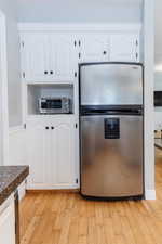 Kitchen with light hardwood / wood-style floors, stainless steel refrigerator, and white cabinetry