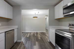 Kitchen featuring white cabinetry, dark wood-type flooring, hanging light fixtures, and appliances with stainless steel finishes