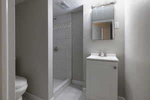 Bathroom with vanity, tiled shower, tile patterned floors, toilet, and a textured ceiling