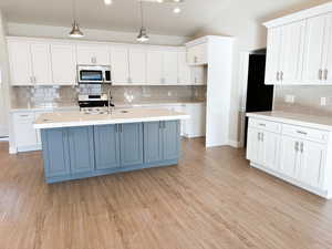 Kitchen featuring decorative light fixtures, white cabinetry, stainless steel appliances, and a kitchen island with sink