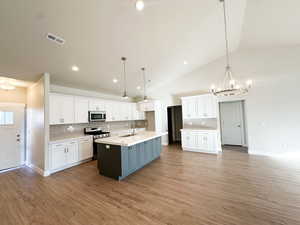 Kitchen with white cabinetry, hanging light fixtures, stainless steel appliances, tasteful backsplash, and an island with sink