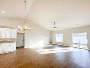 Unfurnished living room with ceiling fan with notable chandelier, light hardwood / wood-style floors, and lofted ceiling