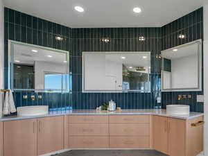 Owner's suite bath with tile walls, tile patterned floors, backsplash, and dual bowl vanity