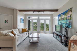 Carpeted living room featuring beam ceiling, french doors, and rail lighting