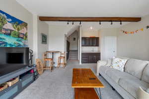 Carpeted living room featuring sink, beam ceiling, and track lighting