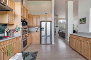 Kitchen with backsplash, light brown cabinets, appliances with stainless steel finishes, and light wood-type flooring