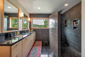 Bathroom featuring tiled shower, tile patterned flooring, tile walls, and double sink vanity