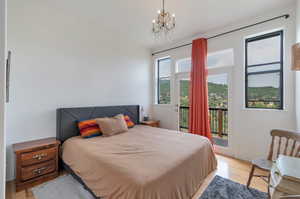 Bedroom with an inviting chandelier, access to exterior, multiple windows, and light wood-type flooring