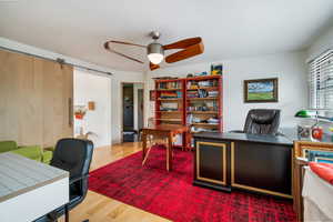 Office with wood-type flooring, a barn door, and ceiling fan