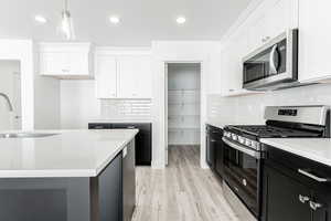 Kitchen with white cabinetry, light hardwood / wood-style floors, appliances with stainless steel finishes, and pendant lighting