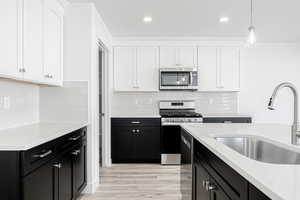 Kitchen with white cabinets, hanging light fixtures, appliances with stainless steel finishes, light hardwood / wood-style floors, and sink