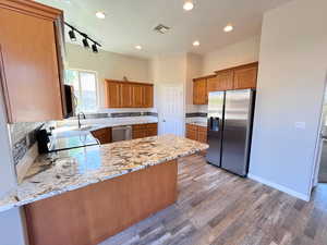 Kitchen featuring backsplash, track lighting, light stone countertops, appliances with stainless steel finishes, and wood-type flooring