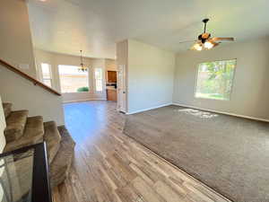 Unfurnished living room with a textured ceiling, carpet flooring, and ceiling fan with notable chandelier