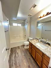 Full bathroom with a textured ceiling, toilet, vanity,  shower combination, and hardwood / wood-style flooring