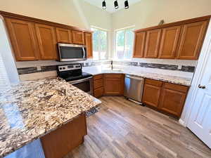 Kitchen with hardwood / wood-style flooring, stainless steel appliances, light stone counters, and sink