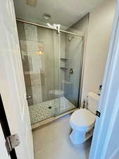 Bathroom with tile patterned flooring, a shower with shower door, and toilet