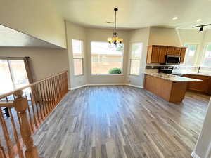 Kitchen featuring an inviting chandelier, light stone counters, pendant lighting, stainless steel appliances, and hardwood / wood-style flooring