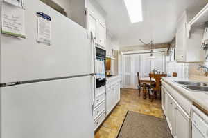 Kitchen featuring white cabinetry, white appliances, sink, and pendant lighting