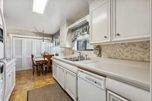 Kitchen featuring light tile patterned floors, white cabinets, white dishwasher, decorative light fixtures, and sink