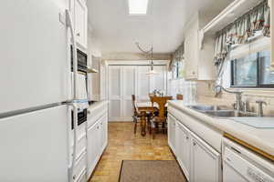 Kitchen with light tile patterned flooring, pendant lighting, white cabinets, white appliances, and sink