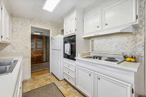 Kitchen featuring sink, white appliances, light tile patterned floors, and white cabinets