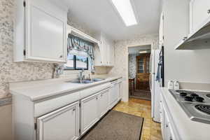 Kitchen with light tile patterned flooring, white cabinets, wall chimney exhaust hood, sink, and white dishwasher