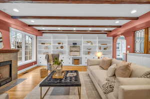 Living room featuring light hardwood / wood-style floors, a tile fireplace, beamed ceiling, and a healthy amount of sunlight