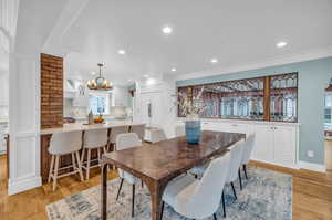 Dining space featuring sink, brick wall, light hardwood / wood-style flooring, and ornamental molding