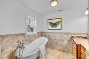 Primary Bathroom featuring a tub, vanity, tile patterned floors, and tile walls