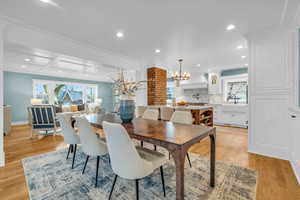 Dining room with sink, light wood-type flooring, brick wall, a notable chandelier, and coffered ceiling