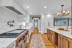 Kitchen with white cabinetry, tasteful backsplash, light hardwood / wood-style floors, decorative light fixtures, and high end appliances