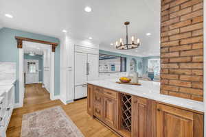 Kitchen featuring crown molding, light wood-type flooring, light stone countertops, and decorative light fixtures