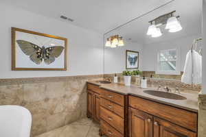 Primary Bathroom with tile walls, dual vanity, tile patterned floors, and a bathing tub