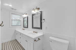 Bathroom featuring tile patterned floors, double vanity, tile walls, and toilet