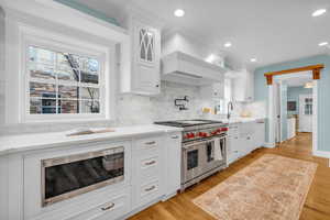 Kitchen featuring light hardwood / wood-style floors, white cabinetry, decorative backsplash, and stainless steel appliances