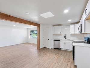 Kitchen featuring white cabinetry, stainless steel appliances, a skylight, sink, and light hardwood / wood-style floors