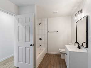 Full bathroom featuring vanity, tiled shower / bath combo, wood-type flooring, and toilet