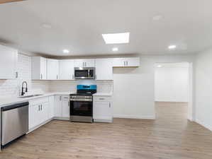 Kitchen with sink, light wood-type flooring, stainless steel appliances, and white cabinets