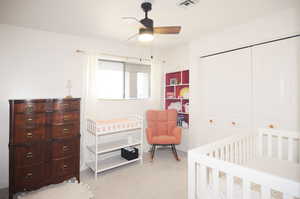 Carpeted bedroom with a crib, a closet, and ceiling fan