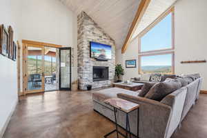 Living room with plenty of natural light, high vaulted ceiling, a stone fireplace, and concrete floors