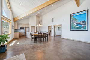 Dining room with beamed ceiling, an inviting chandelier, sink, high vaulted ceiling, and concrete floors