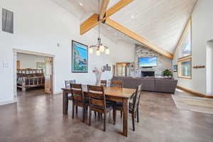 Dining area with beam ceiling, a stone fireplace, a chandelier, and high vaulted ceiling