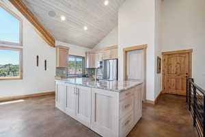 Kitchen featuring stainless steel fridge, sink, light stone counters, backsplash, and high vaulted ceiling