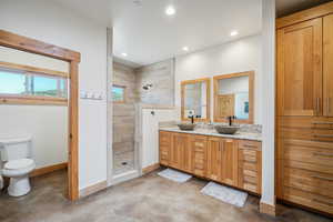 Bathroom featuring tiled shower, double vanity, toilet, and concrete floors