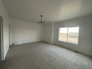 Carpeted empty room featuring a notable chandelier and a textured ceiling