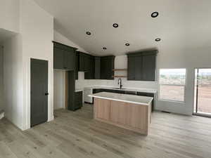 Kitchen featuring sink, a center island, lofted ceiling, and light wood-type flooring