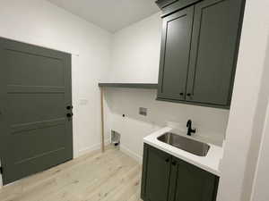 Clothes washing area featuring sink, cabinets, light hardwood / wood-style floors, hookup for an electric dryer, and washer hookup