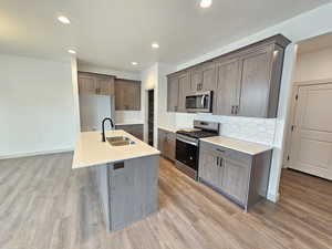 Kitchen with light hardwood / wood-style floors, sink, a kitchen island with sink, and stainless steel appliances