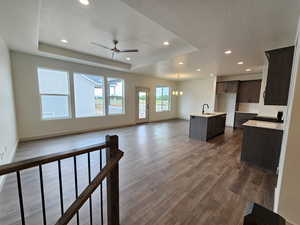 Living room with dark hardwood / wood-style floors, a raised ceiling, ceiling fan with notable chandelier, and sink