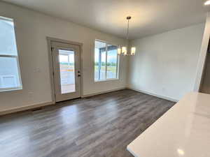 Unfurnished dining area with dark wood-type flooring and a notable chandelier